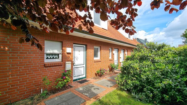 Une maison en briques avec une porte verte, un petit jardin et un ciel dégagé.