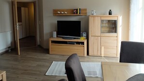 Olohuone, jossa on televisio, puinen kaappi ja ovi, joka johtaa toiseen huoneeseen.