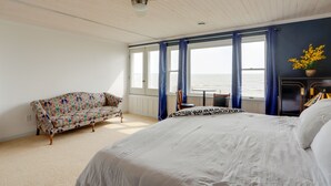 Ein Schlafzimmer mit einem großen Bett, einer Couch, einem kleinen Tisch und Meerblick durch die Fenster.