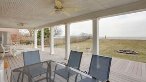 Eine überdachte Terrasse im Freien mit einem Glastisch und Stühlen, weißen Säulen und Blick auf den Ozean.