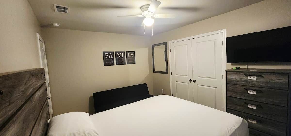 A bedroom with a bed, a ceiling fan, a wardrobe, and a TV.