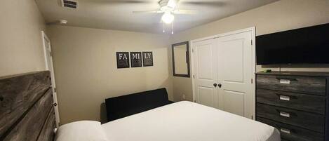 A bedroom with a bed, a ceiling fan, a wardrobe, and a TV.
