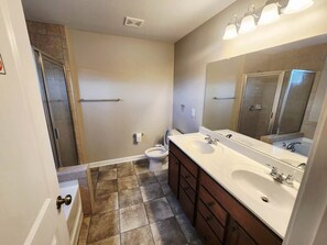 A bathroom with a shower, toilet, and double sink vanity.