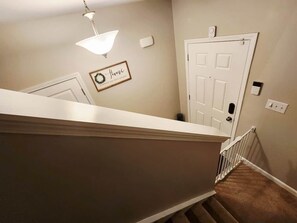 Una escalera con barandilla blanca, un accesorio de iluminación, una puerta y un cartel fijado a la pared.