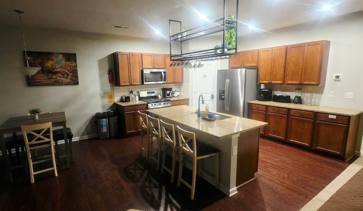 A modern kitchen with wooden cabinets, a central island with bar stools, a microwave, oven, and refrigerator.