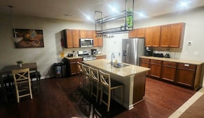 Una cocina moderna con armarios de madera, una isla central con taburetes de bar, microondas, horno y refrigerador.