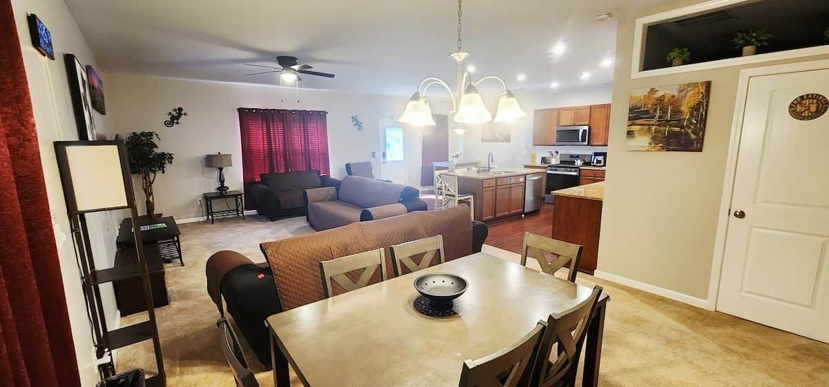 A living room with a sofa, dining table, and chairs, a kitchen area with a microwave, and a door with a circular emblem.