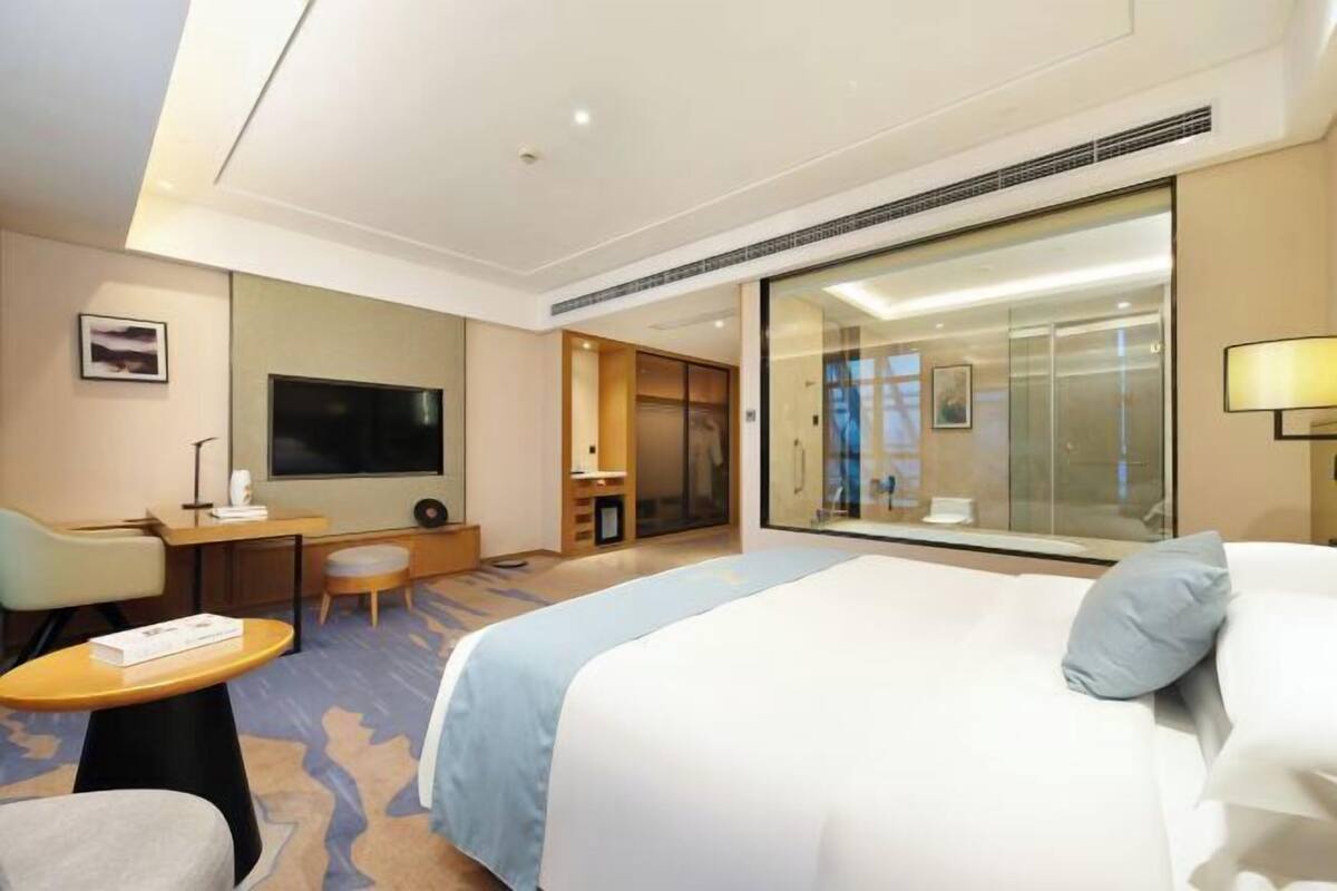 Una habitación de hotel con cama, escritorio, silla, televisor y un amplio ventanal.