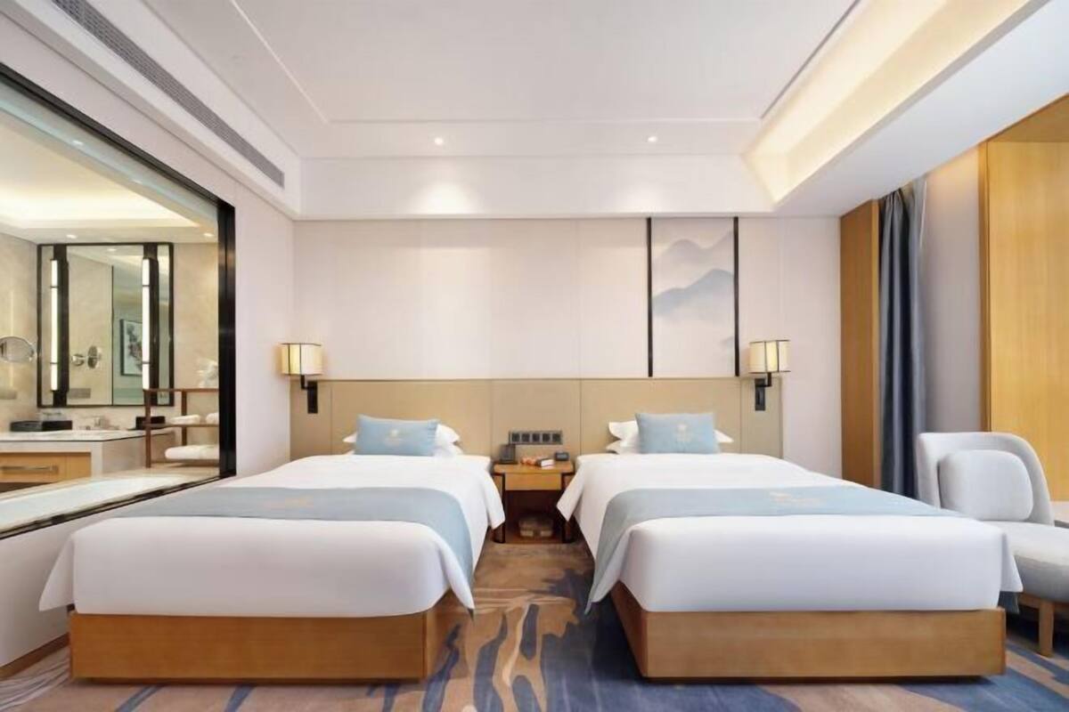 Habitación de hotel con dos camas, un espejo grande, una mesita de noche y vistas a la ciudad.