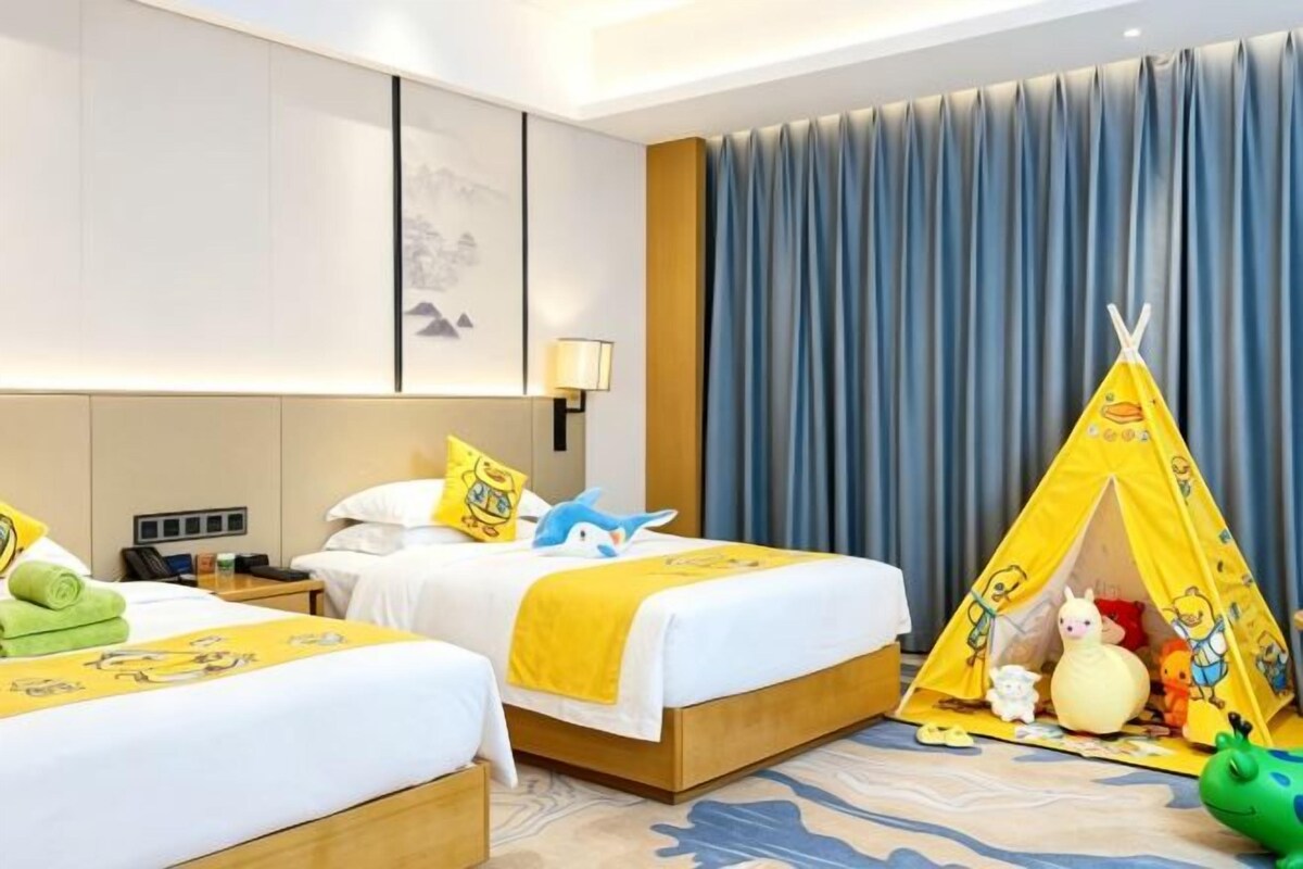 A hotel room with two beds, a play tent, and a wall-mounted lamp.