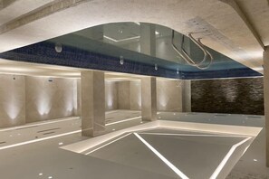 Une piscine intérieure moderne dotée d’un toit en verre et d’un motif géométrique au niveau du sol.