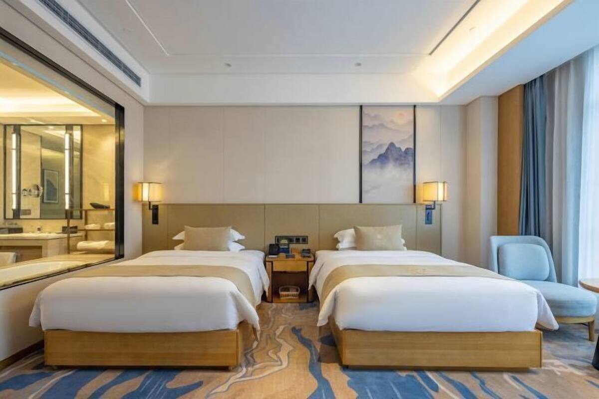 Habitación de hotel con dos camas, un espejo grande, una mesita de noche y vistas a la montaña.