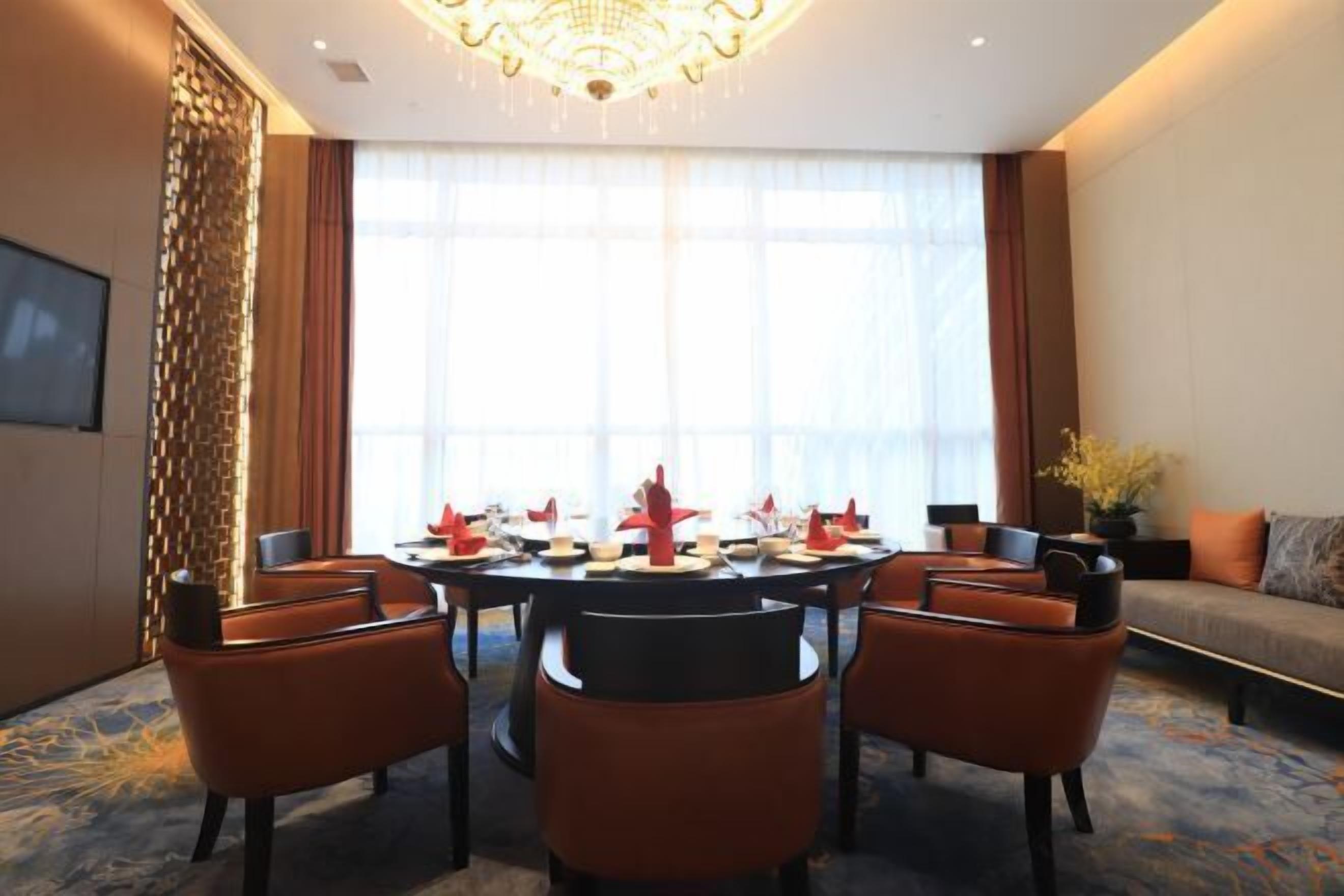 A modern dining area with a round table set for six, surrounded by orange chairs.