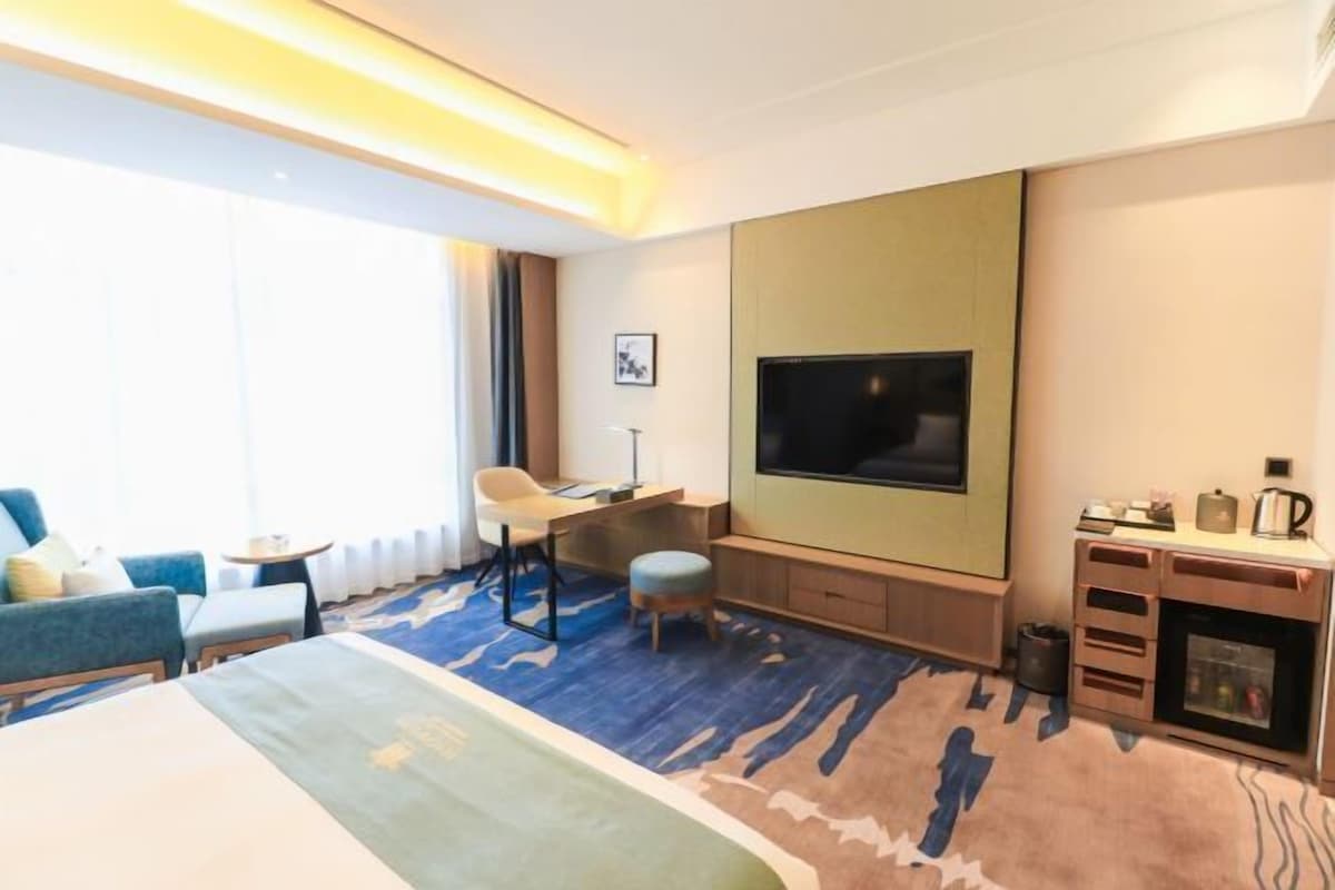 A hotel room with a bed, a desk, a chair, a TV, and a minibar.