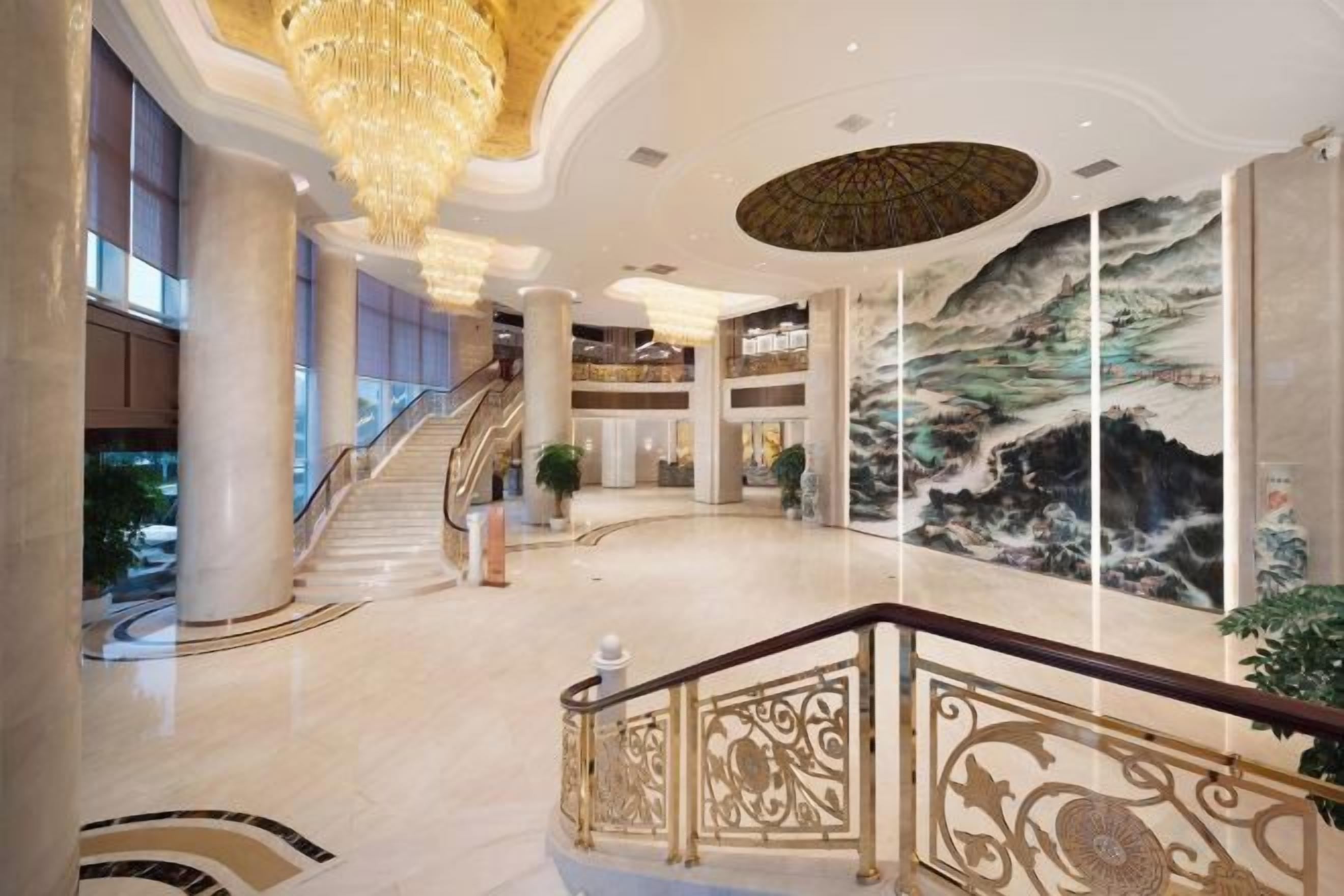 A spacious lobby with a grand staircase, a large mural, and a chandelier.