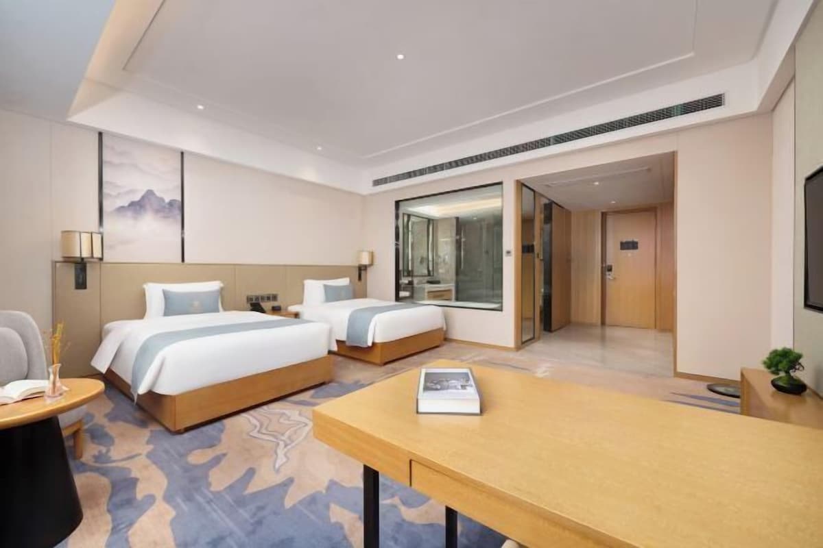 A hotel room with two beds, a desk, a chair, a TV, and a large window.