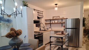 A modern kitchen with a stainless steel refrigerator, a dining table with placemats, and a vase with dried flowers.