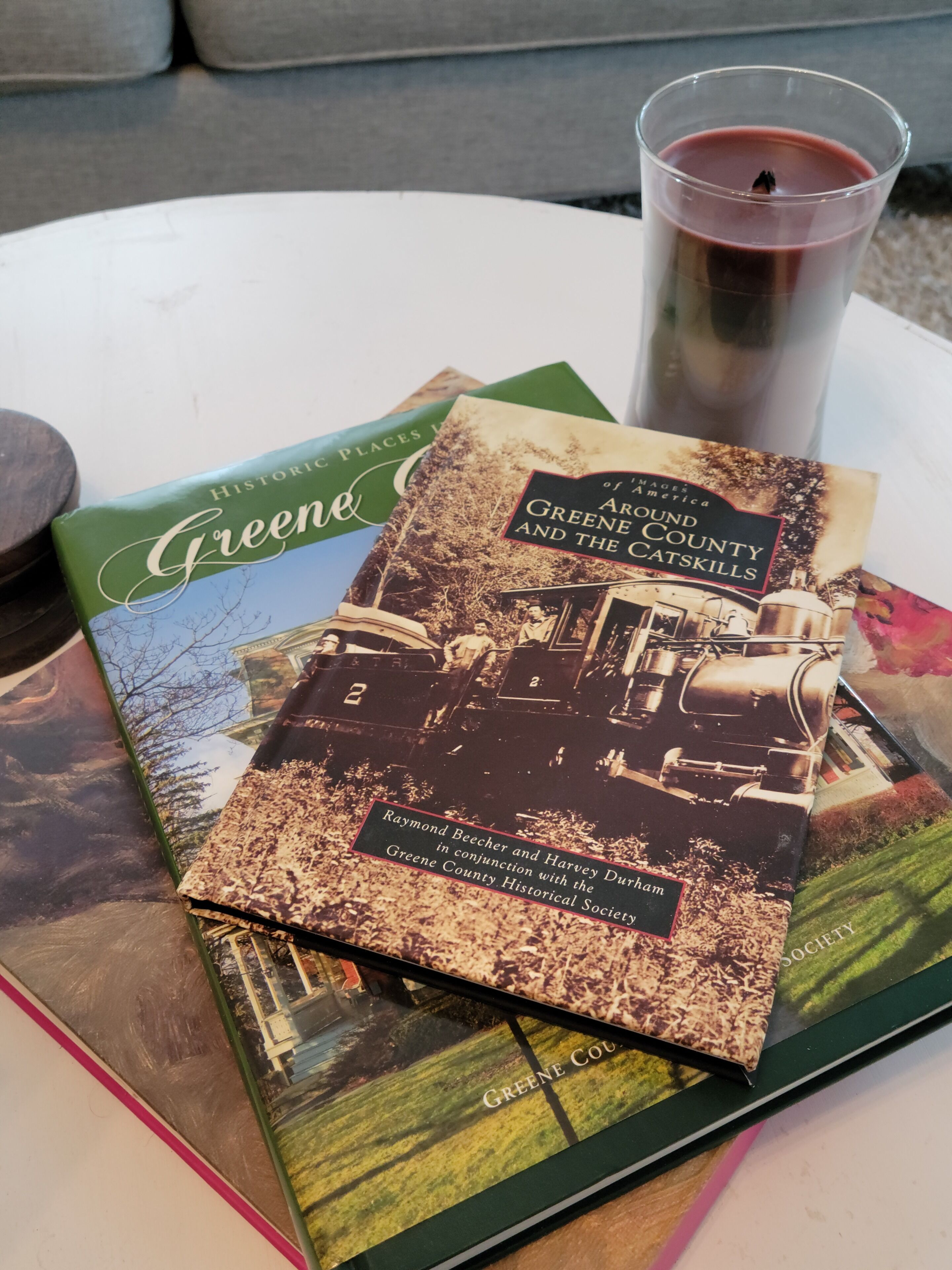 Kirja, jonka nimi on ”Greene County ja Catskills”, ja jonka kannessa on historiallinen valokuva, on asetettu pöydälle kynttilän viereen.