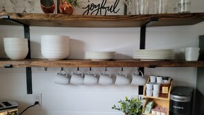 A kitchen with wooden shelves holding white bowls, plates, and mugs. There is a coffee maker and a toaster on the counter.