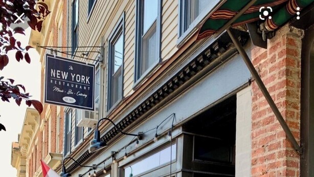 A restaurant with outdoor seating, a sign for 'The New York Restaurant', and a nearby antique shop.