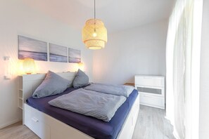 Een slaapkamer met een bed, nachtkastjes, een hanglamp en wanddecoratie.