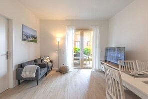 A modern living room with a sofa, a dining table with chairs, a TV, and a sliding glass door leading to an outdoor area. - Vacations directly on the south beach - Ferien am Südstrand (Wyk auf Föhr)
