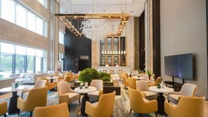 Un hall d’hôtel moderne avec des chaises jaunes, un grand lustre et un téléviseur fixé au mur.