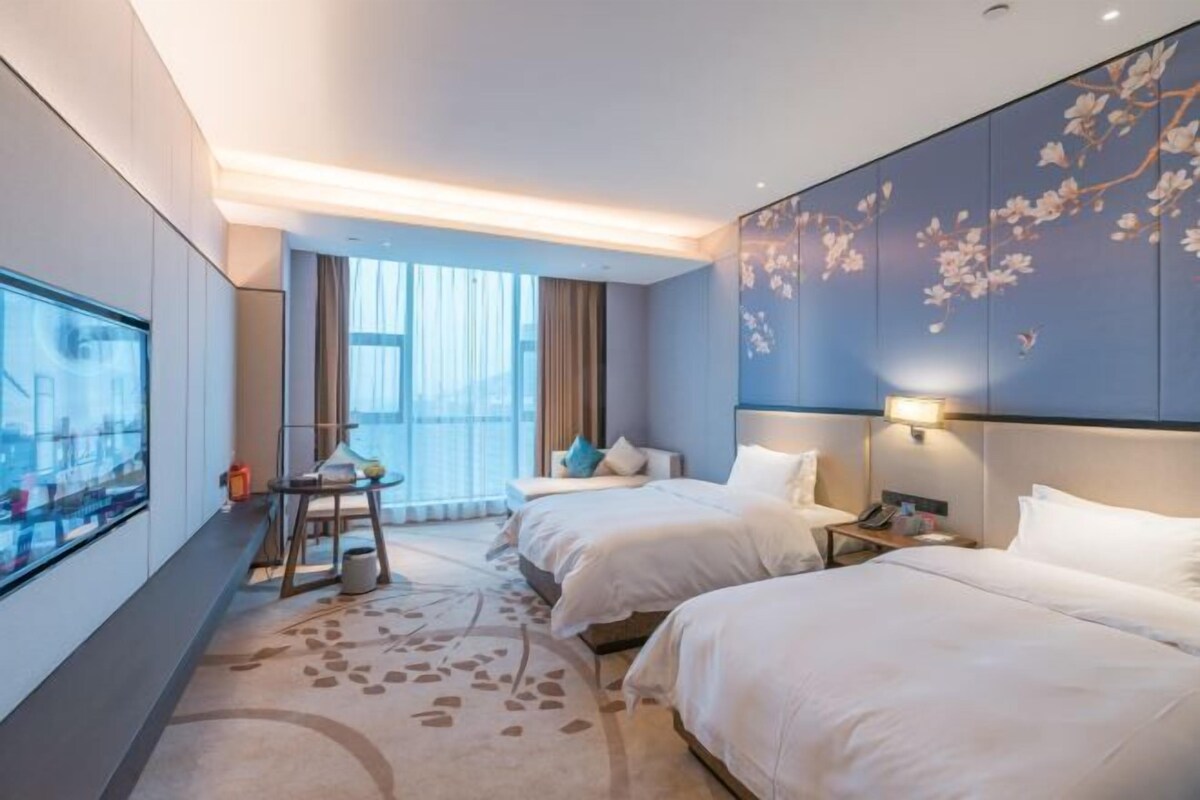 Ein modernes Hotelzimmer mit zwei Betten, einem großen Fenster und einer Wanddekoration.