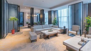 Un salon moderne avec un canapé, une table basse et des fauteuils, de grandes fenêtres et une plante en pot.