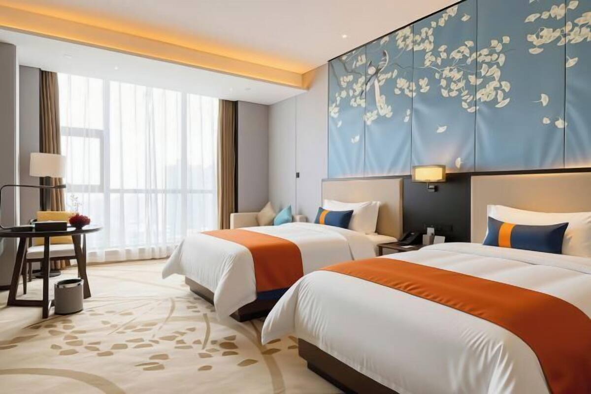 A hotel room with two beds, a desk, a lamp, and a large floral-patterned headboard.