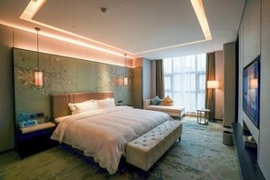 Ein modernes Hotelzimmer mit einem großen Bett, einer Bank, einem Fernseher und Blick auf die Stadt durch das Fenster.