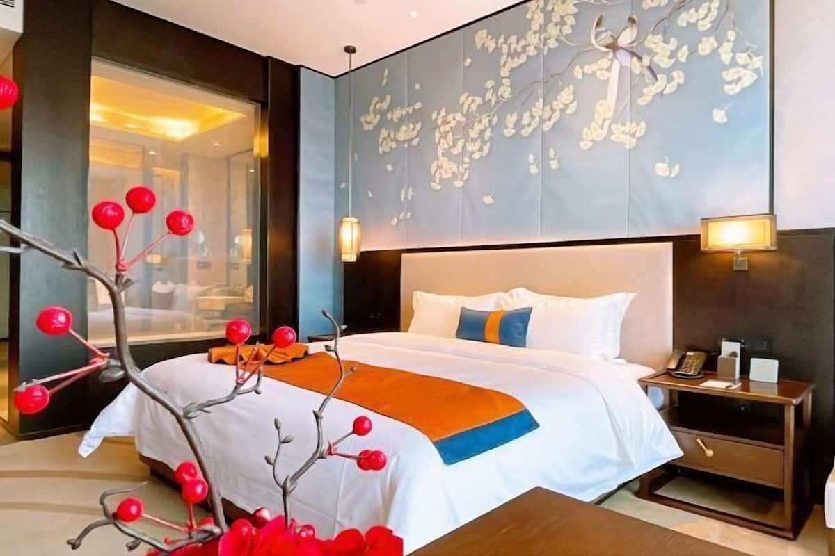 Une chambre d’hôtel avec un grand lit, une table de chevet, une lampe fixée au mur et une branche décorative ornée de baies rouges.