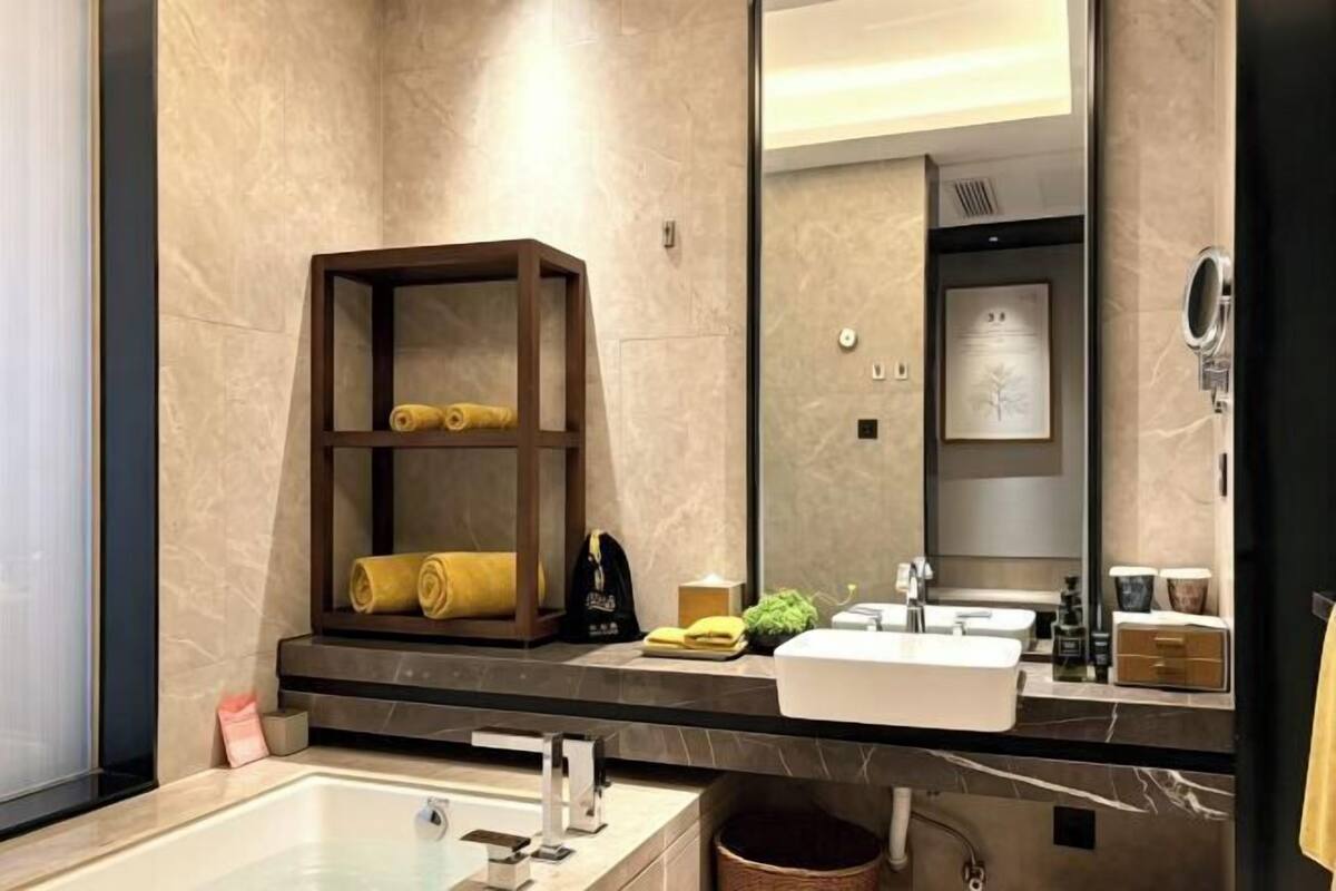 A modern bathroom with a large mirror, a bathtub, a sink, and a shelf with towels.