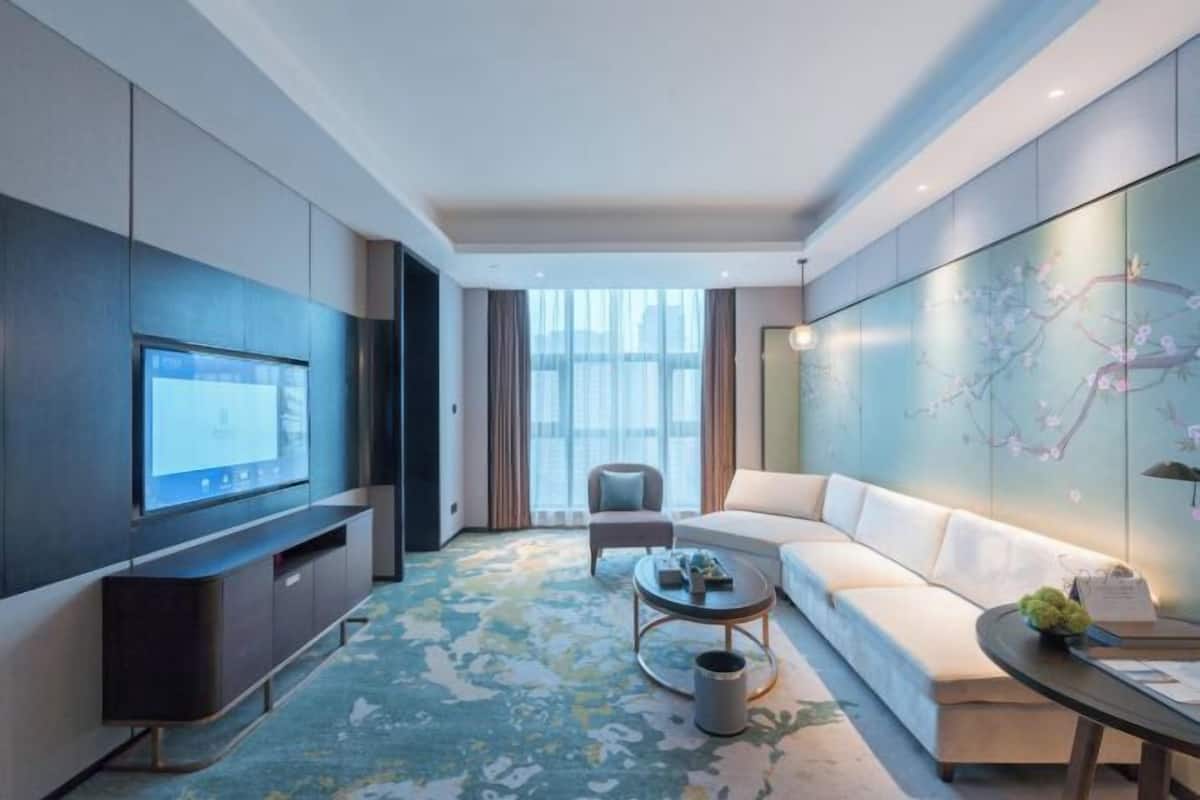 Une chambre d’hôtel moderne dotée d’un grand téléviseur à écran plat, d’un canapé, d’une table basse et d’un mur décoratif.