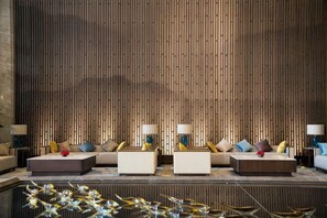 A modern hotel lobby with a vertical wooden panel wall, three sofas with side tables, and decorative lamps.