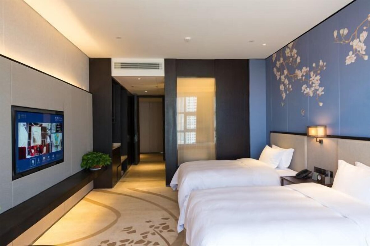 Ein modernes Hotelzimmer mit zwei Betten, einem flachbildfernseher an der Wand und einer dekorativen Wandverkleidung.