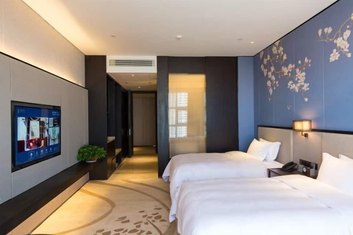 A modern hotel room with two beds, a flat-screen TV mounted on the wall, and a decorative wall panel.