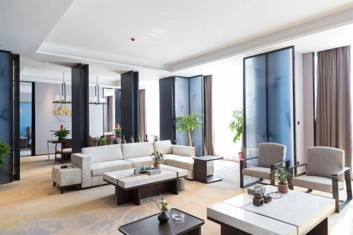 Ein großzügiger Wohnbereich mit Sofa, Couchtisch und Sesseln. Übertöpfe und ein großes Fenster sind ebenfalls vorhanden.