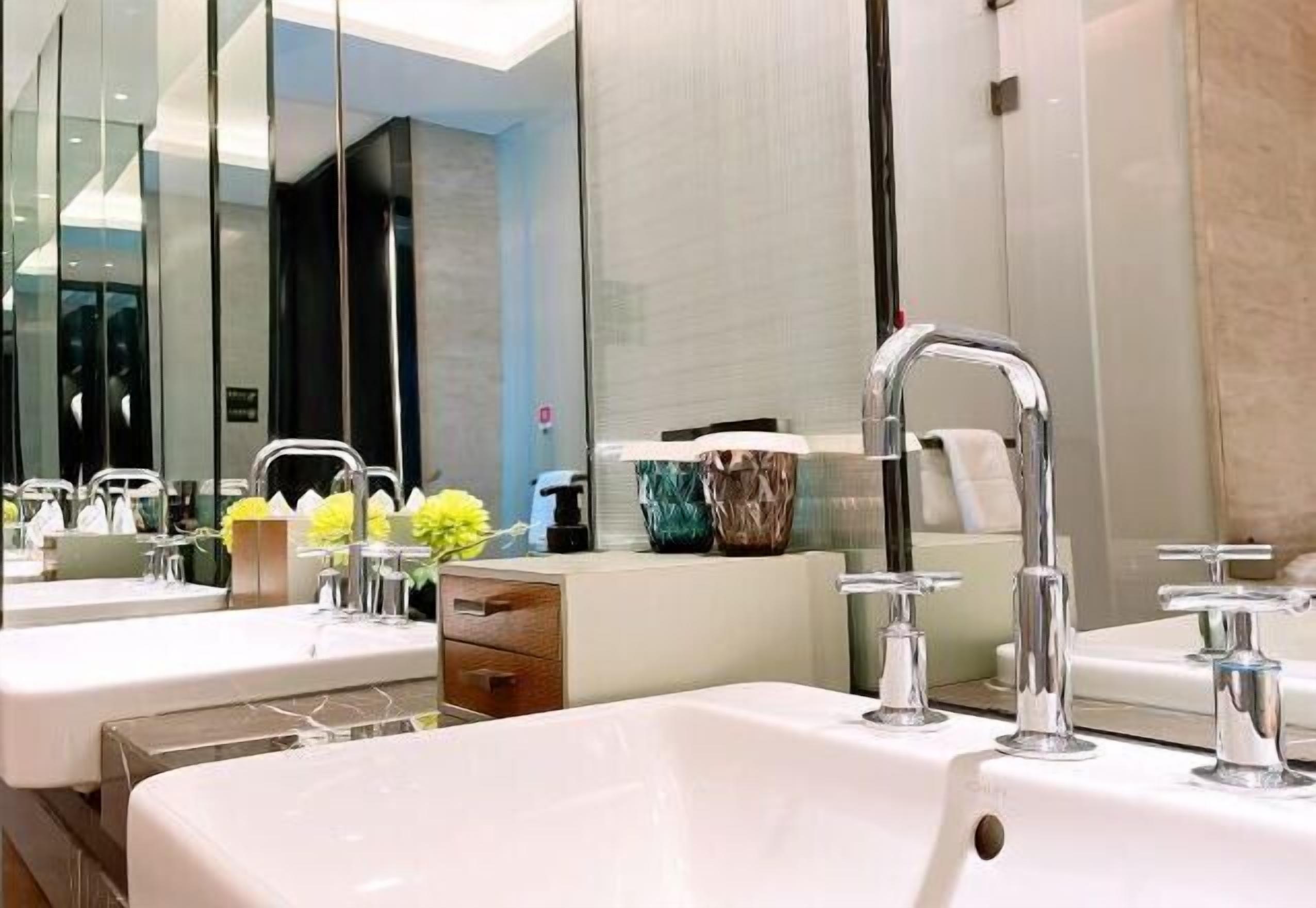 Une salle de bain moderne avec deux lavabos, un miroir et une commode agrémentée d’un vase de fleurs.
