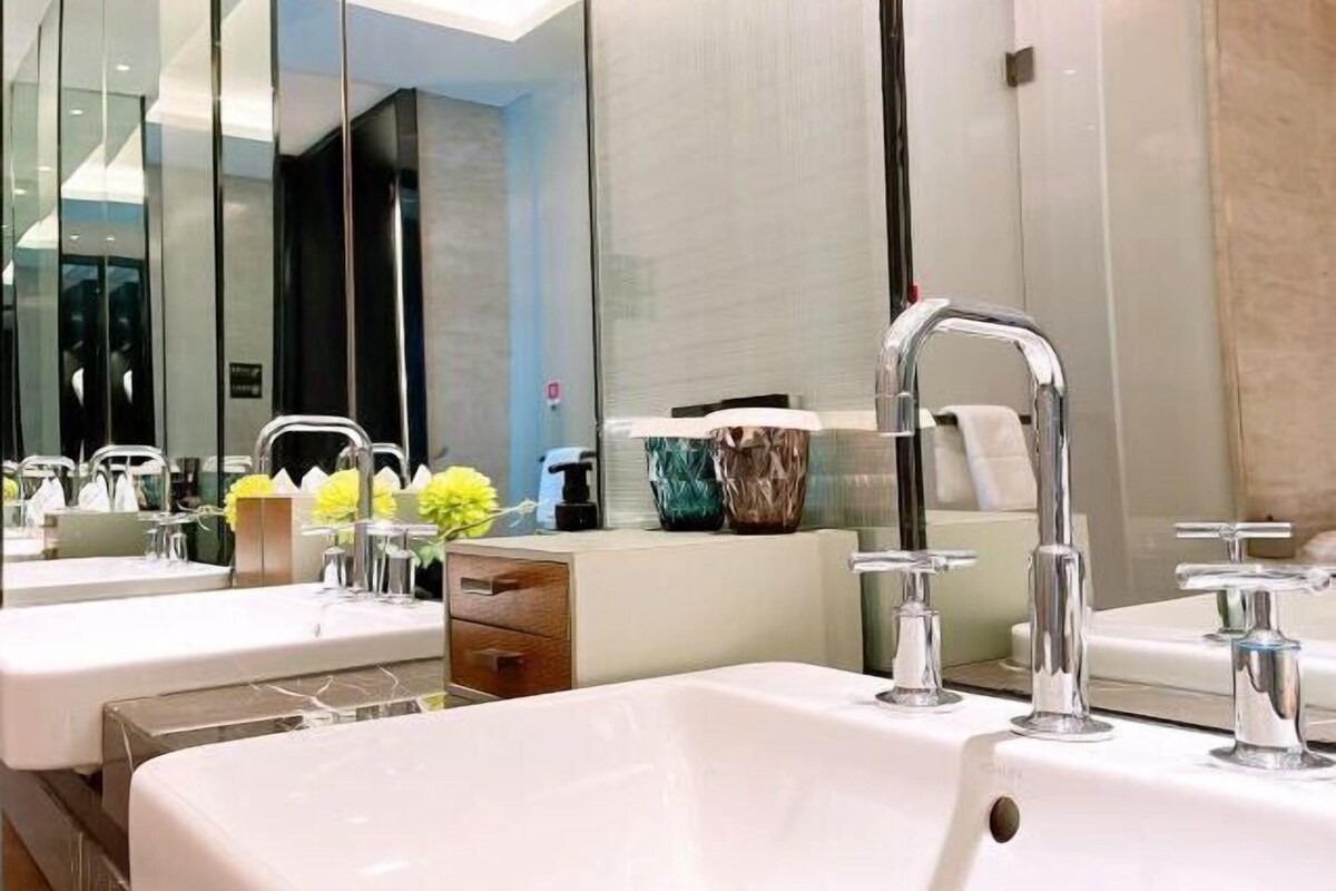 Ein modernes Badezimmer mit zwei Waschbecken, einem Spiegel und einem Waschtisch mit einer Blumenvase.
