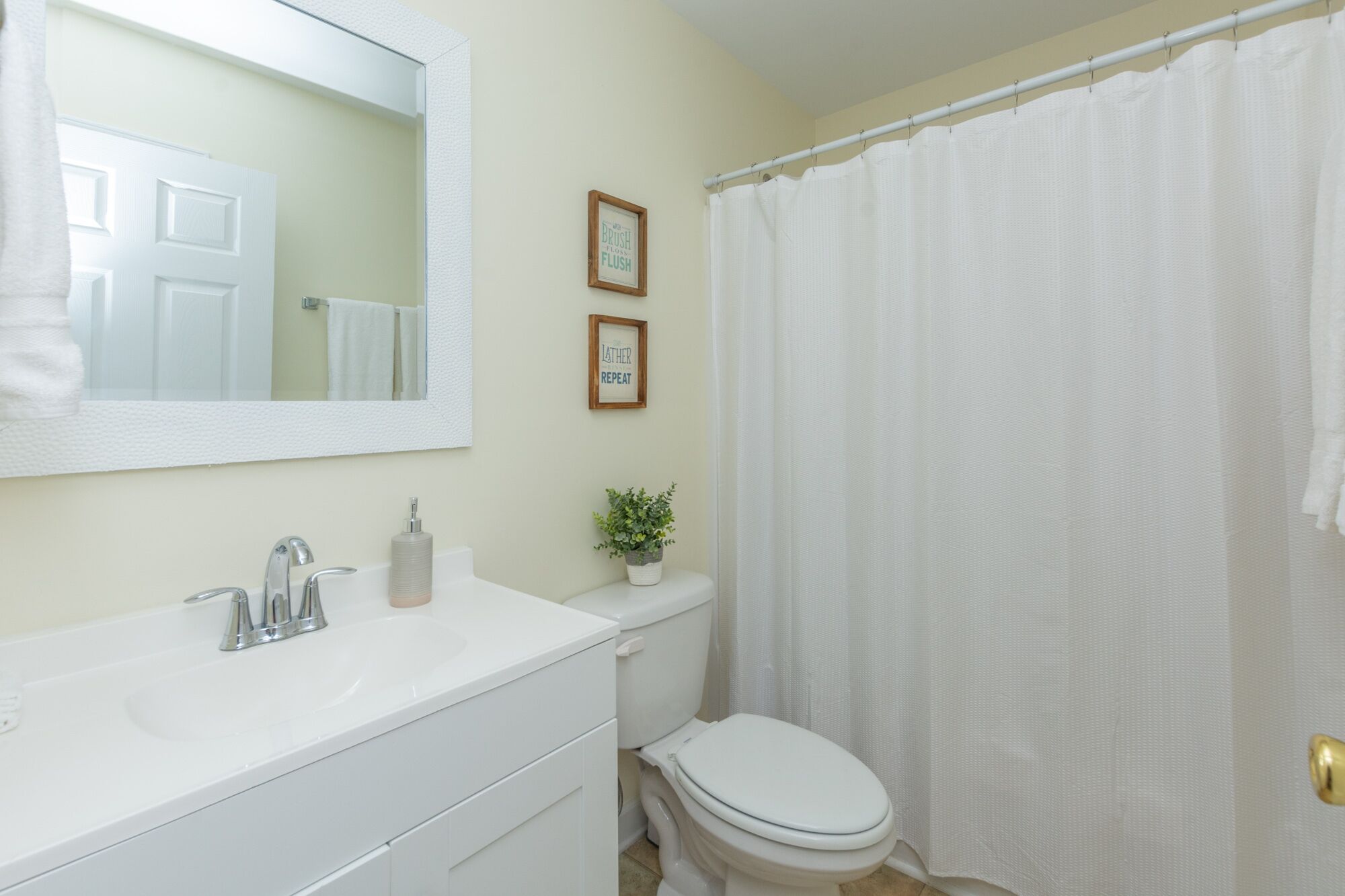 Une salle de bain avec un lavabo blanc, un miroir, des toilettes et un rideau de douche.