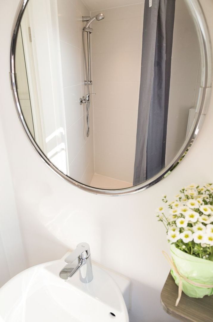 A bathroom with a round mirror, a shower, and a sink.