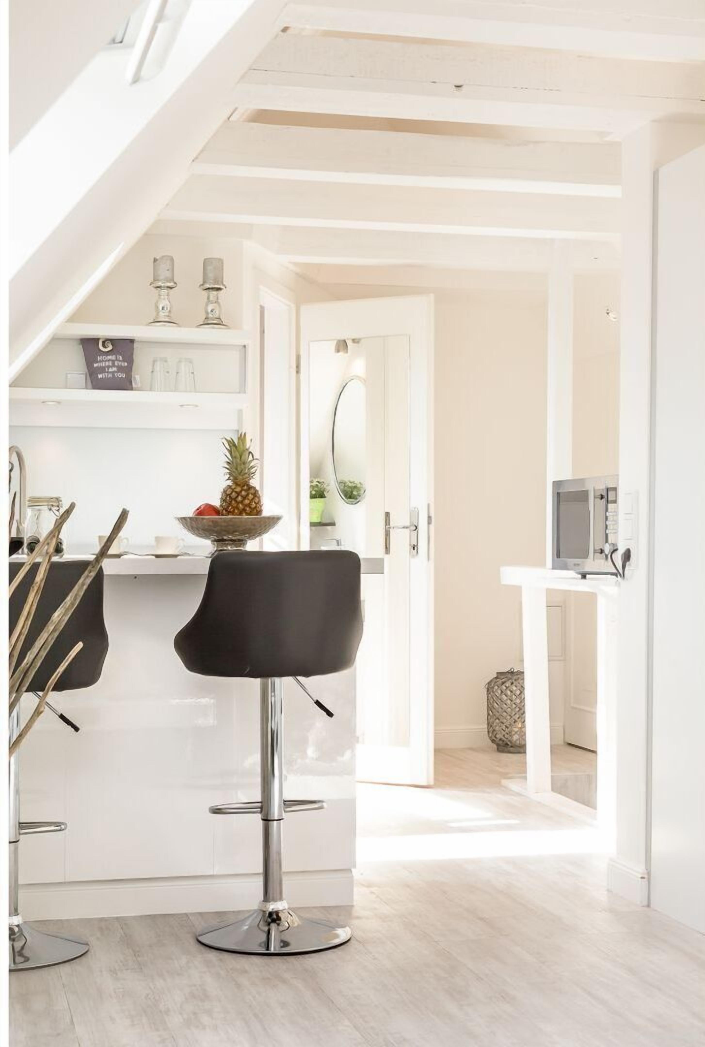 A modern kitchen with two black bar stools, a wooden dining table, and a white countertop.