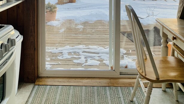 Habitación con puerta corrediza de vidrio que da a una terraza exterior con piso de madera, una silla y una mesa.