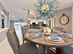 A dining area with a round table set for four, a decorative chandelier, and a wall clock.