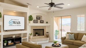 A living room with a fireplace, a television displaying "WELCOME TO WAB WEEKEND AT BERNIES", and a ceiling fan.