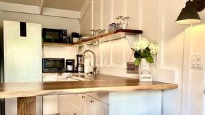 A kitchen with a wooden island, white stools, a microwave, and a coffee maker. - Beautiful Beachside Bungalow (Kailua)