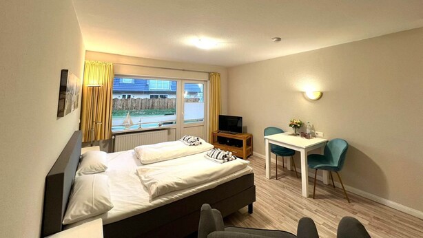 Une chambre d’hôtel avec un lit, un bureau, une chaise, une télévision et une fenêtre avec des rideaux.