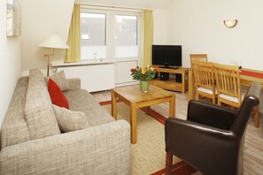 Ein Wohnzimmer mit einer Couch, einem Couchtisch, einem Fernseher und einem kleinen Essbereich mit Stühlen.