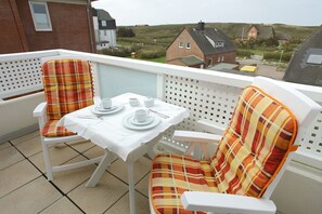 Ein Balkon mit Tisch für zwei Personen, zwei karierten Stühlen und Blick auf Häuser im Hintergrund.